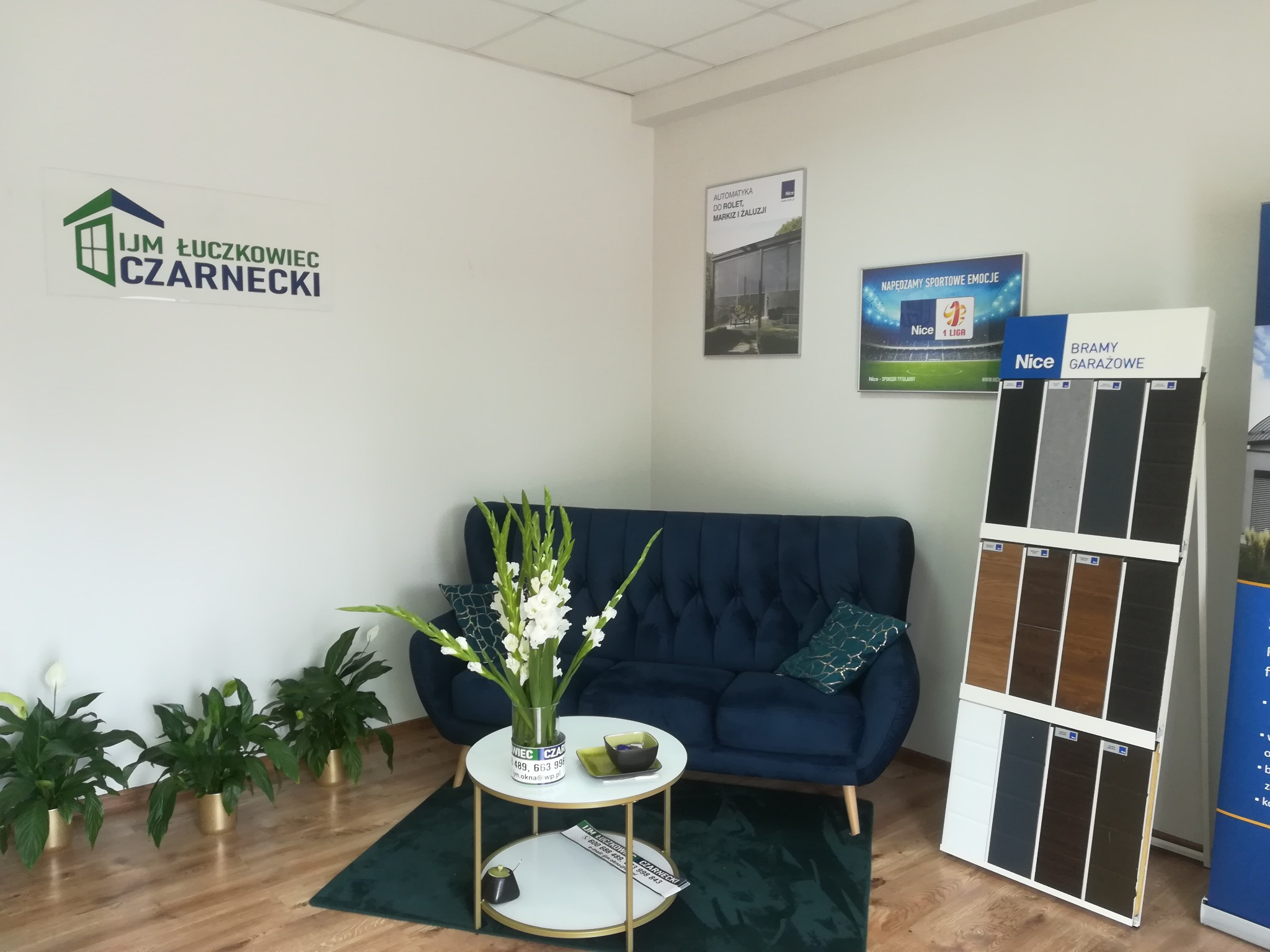 Wnętrze biura firmy IJM Łuczkowiec Czarnecki z ekspozycją próbek bram garażowych Nice, sofą i kwiatami.