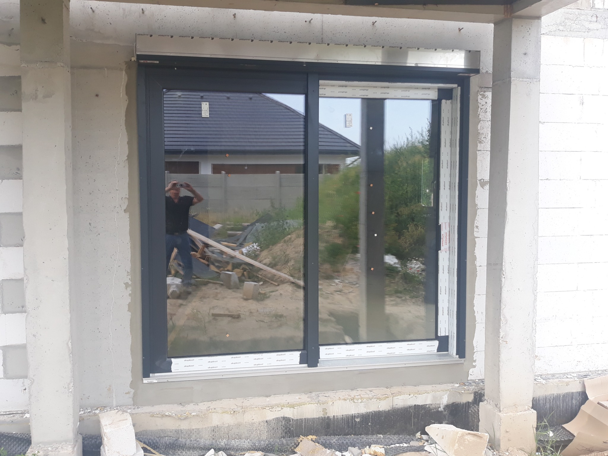 Montaż okna przesuwnego w surowym stanie, widoczny beton komórkowy i odbicie fotografa w szybie.