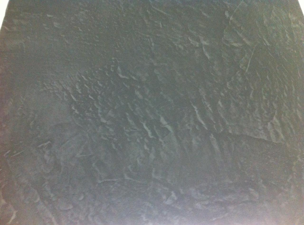 Szara, strukturalna powierzchnia ściany z wyraźnymi, nieregularnymi smugami i delikatnym połyskiem.