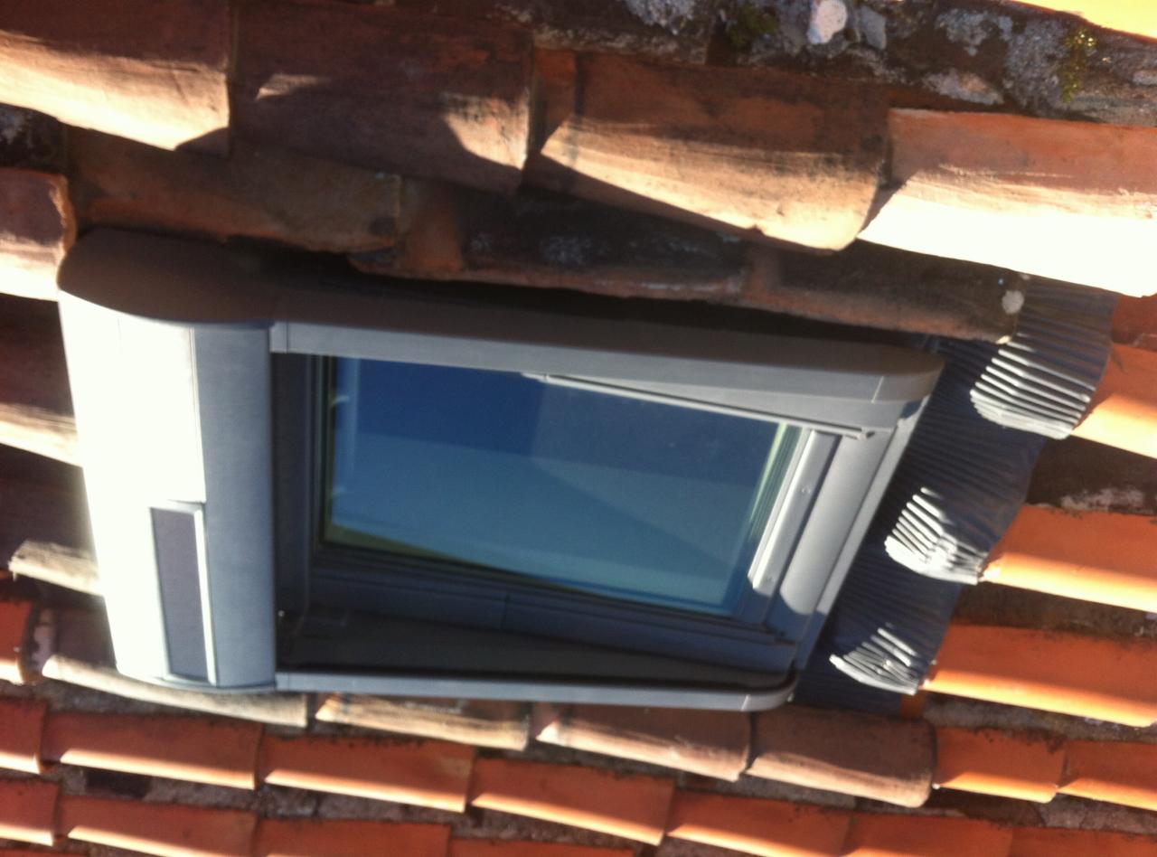 Okno dachowe z szarymi elementami wykończeniowymi wkomponowane w czerwoną dachówkę, widok z góry.