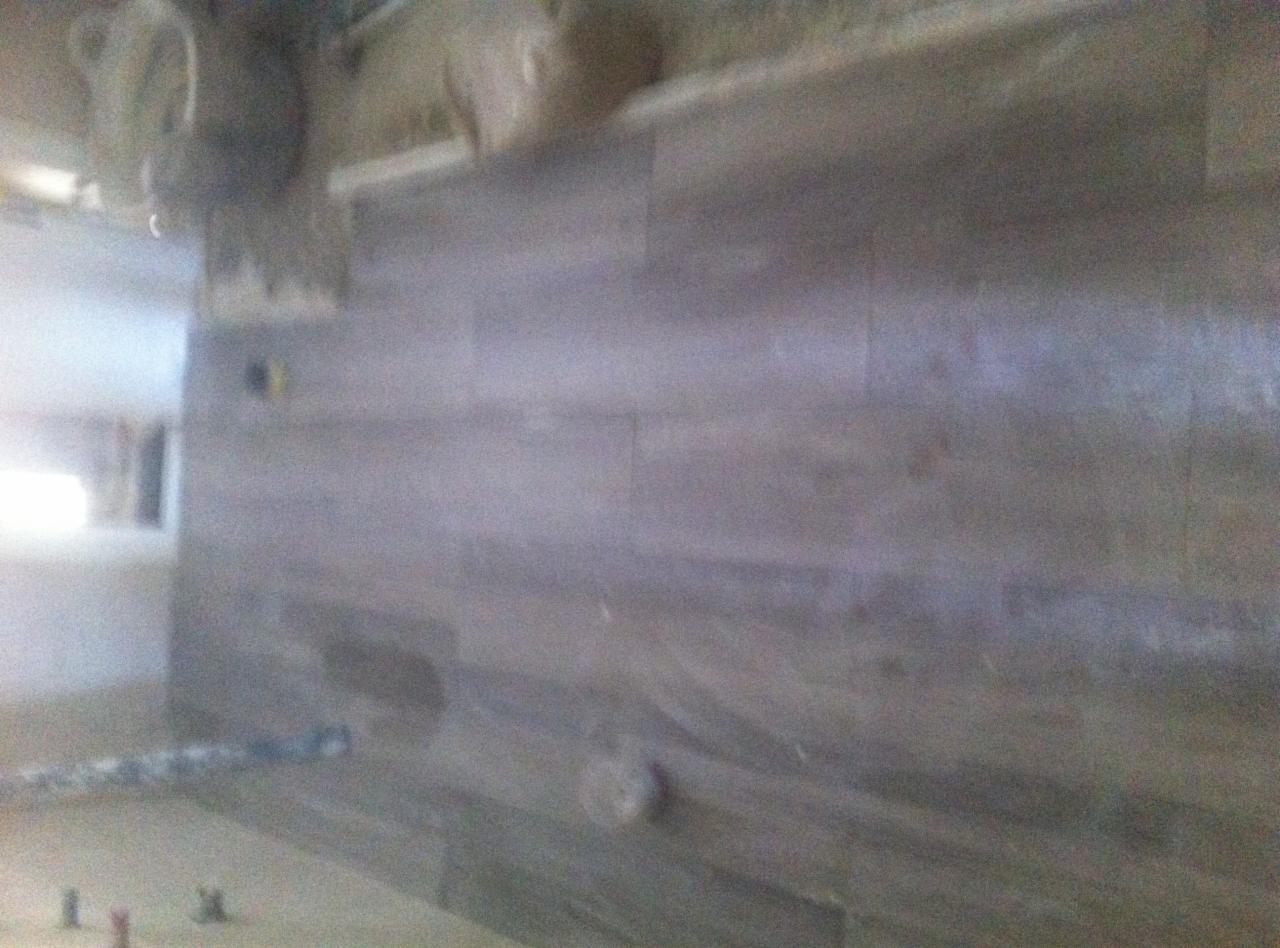 Ściana wyłożona podłużnymi płytkami imitującymi drewno w odcieniach szarości, widoczne elementy instalacji elektrycznej i fragment podłogi z akcesoriami montażowymi.