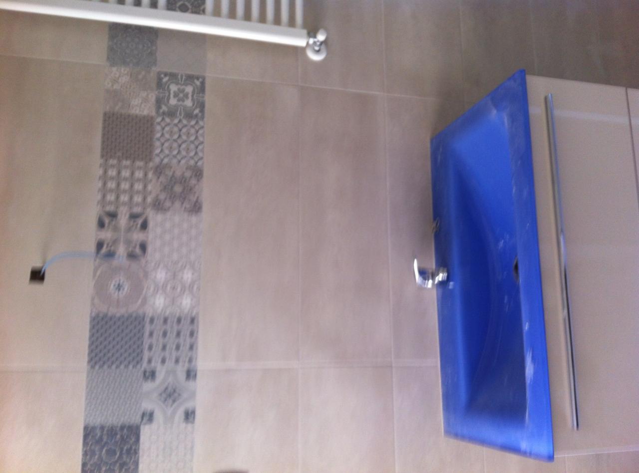 Łazienka po remoncie: niebieska umywalka z chromowaną baterią na tle beżowych płytek z dekoracyjnym pasem patchworkowych wzorów.