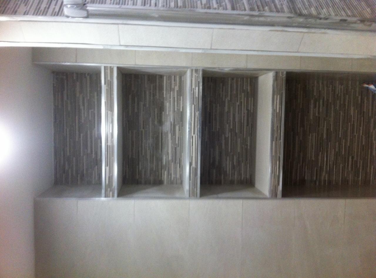 Wnęki ścienne wykończone mozaiką w odcieniach szarości i beżu, z widocznymi pionowymi paskami, osadzone w jasnych, beżowych płytkach.