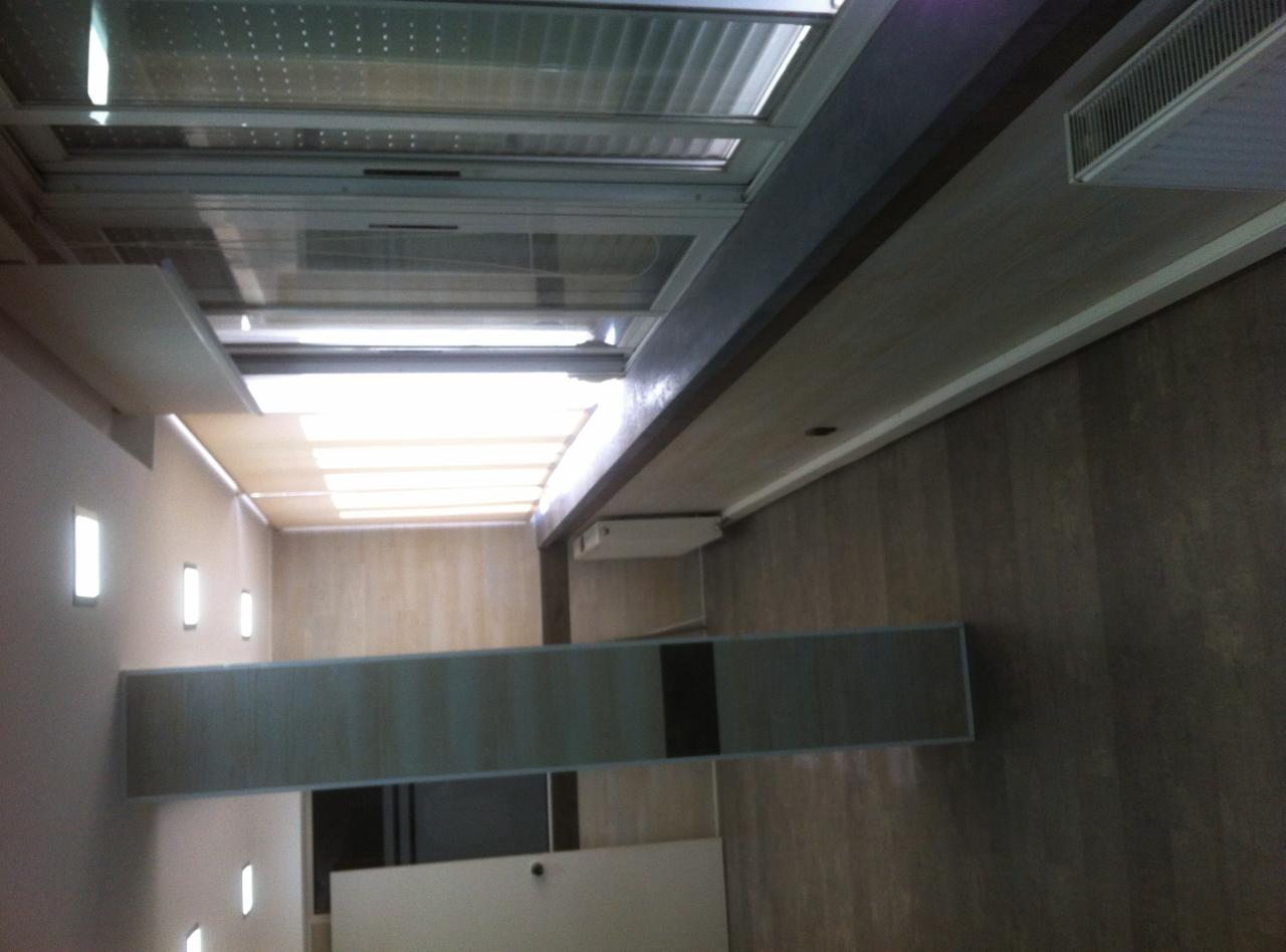 Wnętrze biurowe z oknami dachowymi, oświetleniem LED w ścianach i podwieszanym sufitem z widocznymi elementami wentylacji.