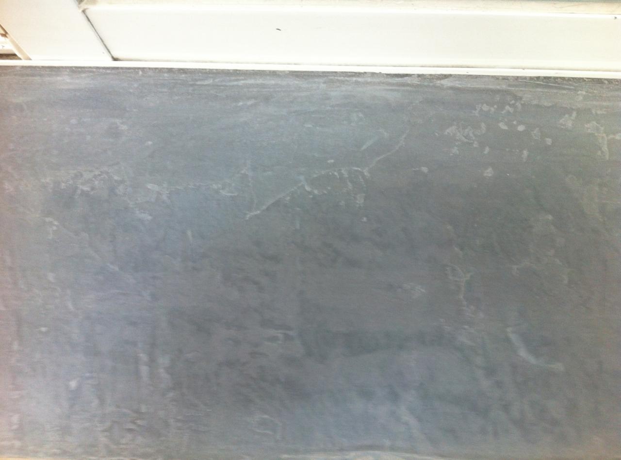 Szara, nierówna powierzchnia ściany z widocznymi smugami i delikatnymi pęknięciami, oświetlona od góry, z fragmentem białego sufitu w górnej części kadru.