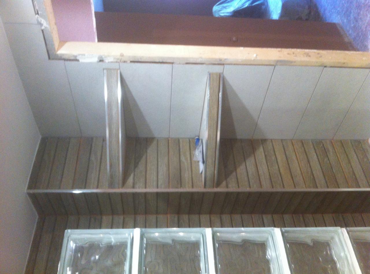 Wnętrze w trakcie prac wykończeniowych: widoczne panele ścienne imitujące drewno, szklane luksfery oraz fragment sufitu z płytami gipsowymi i drewnianą ramą.