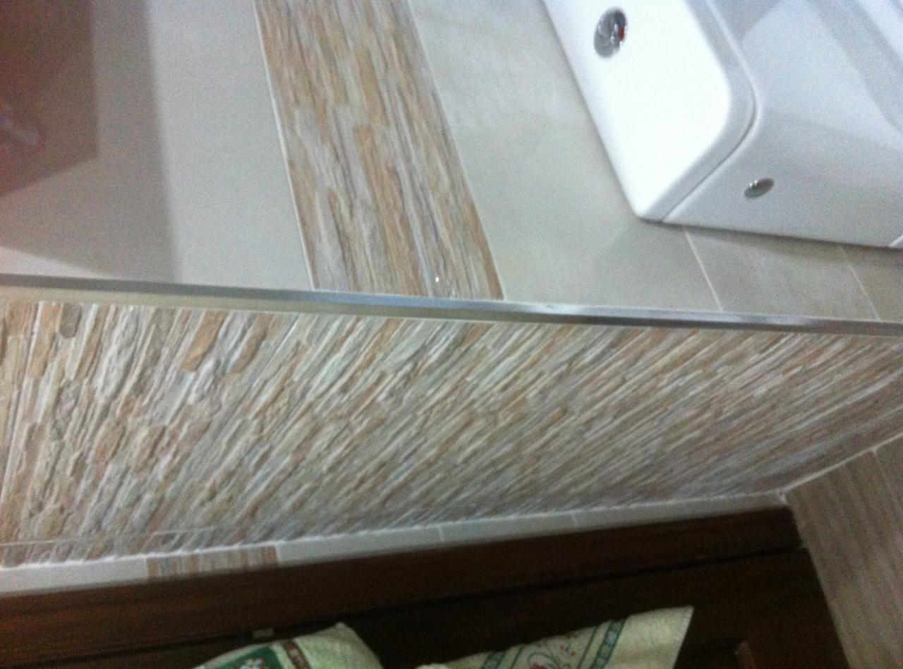 Fragment łazienki z umywalką, ścianą wyłożoną mozaiką z kamienia naturalnego o nieregularnej fakturze i brązową szafką pod umywalką, widoczne z góry pod kątem.