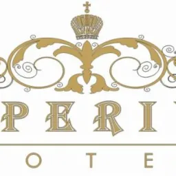 Złote logo Imperium Hotel z koroną i ozdobnymi zawijasami na białym tle.