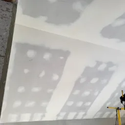 Poddasze w trakcie szpachlowania, widoczne łączenia płyt gipsowo-kartonowych wypełnione masą szpachlową, oświetlone lampą budowlaną.