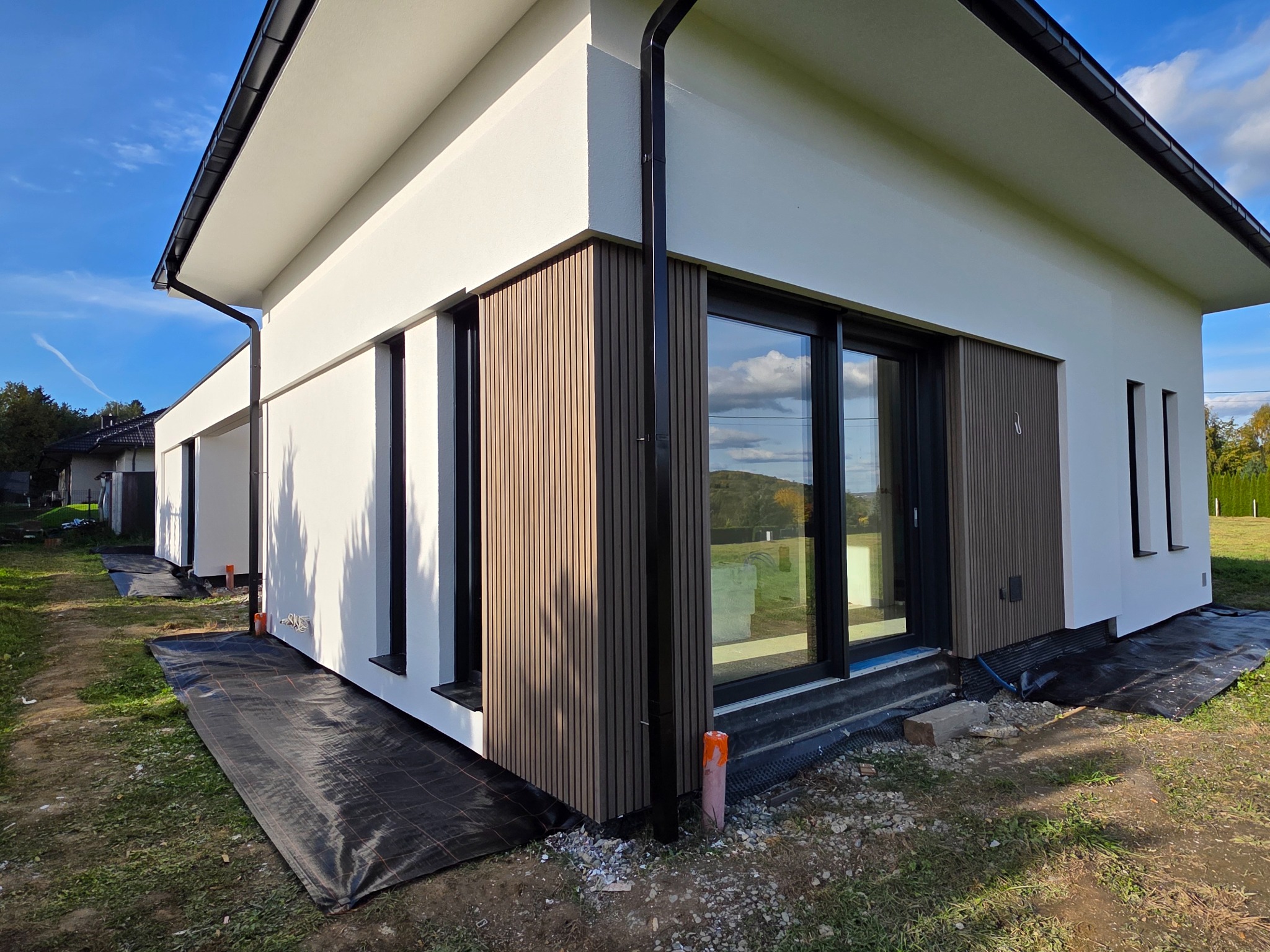 Nowoczesna elewacja domu jednorodzinnego z drewnianymi panelami i białym tynkiem, widok z zewnątrz. Realizacja w Wadowicach.