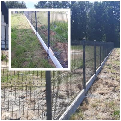 Długi, panelowy, metalowy płot z podmurówką z prefabrykatów betonowych na nierównym terenie, widok z boku.