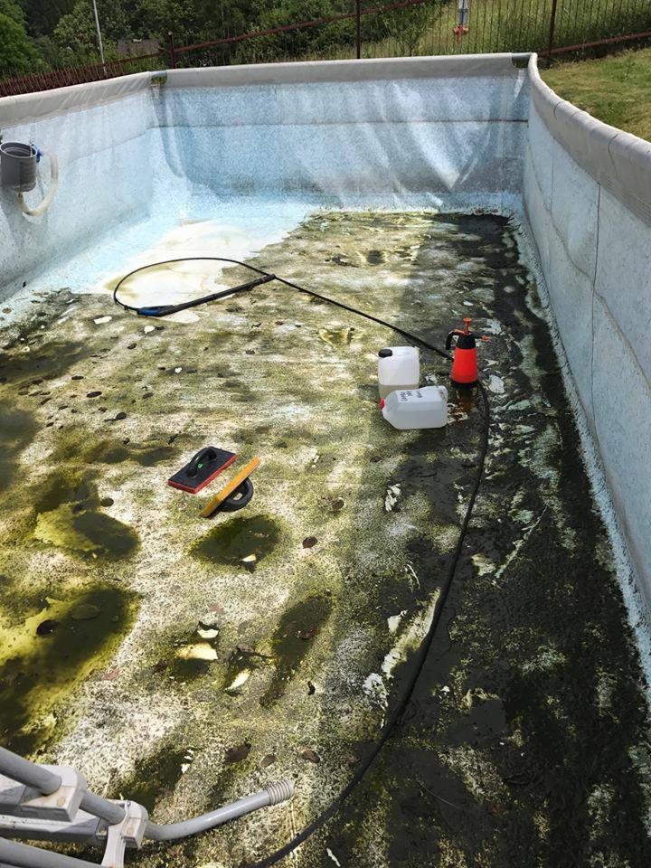 Brudny basen ogrodowy w trakcie czyszczenia: widoczne narzędzia, pompa ciśnieniowa, chemia i resztki organiczne na dnie.