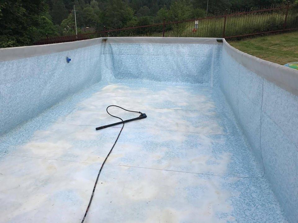 Pusty basen ogrodowy z niebieską mozaiką, przygotowywany do czyszczenia, widoczny wąż do odkurzacza basenowego na dnie.