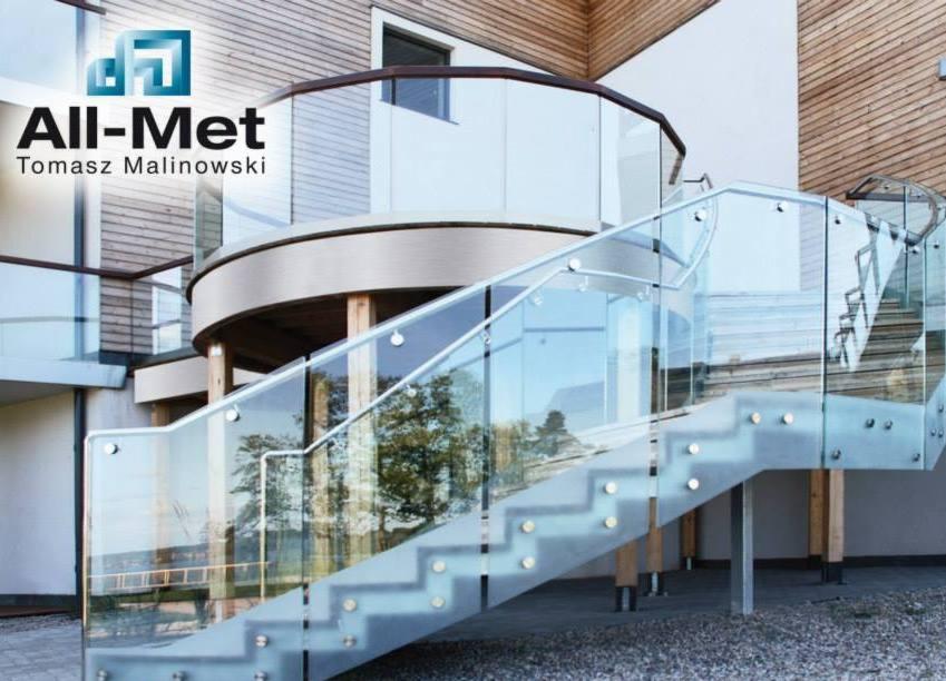 Zewnętrzne schody metalowe z szklaną balustradą prowadzące na balkon domu z drewnianą elewacją, widoczne mocowania stopni.