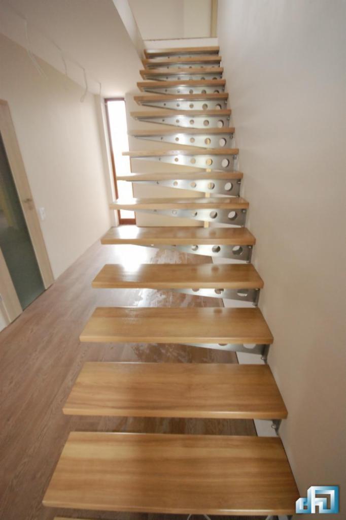 Bieg spiralnych schodów z drewnianymi stopniami i metalowymi wspornikami z otworami, widok z dołu.