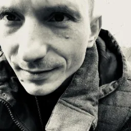 Czarno-białe zdjęcie portretowe mężczyzny z bliska, z widoczną kamizelką i tłem z drzewami.