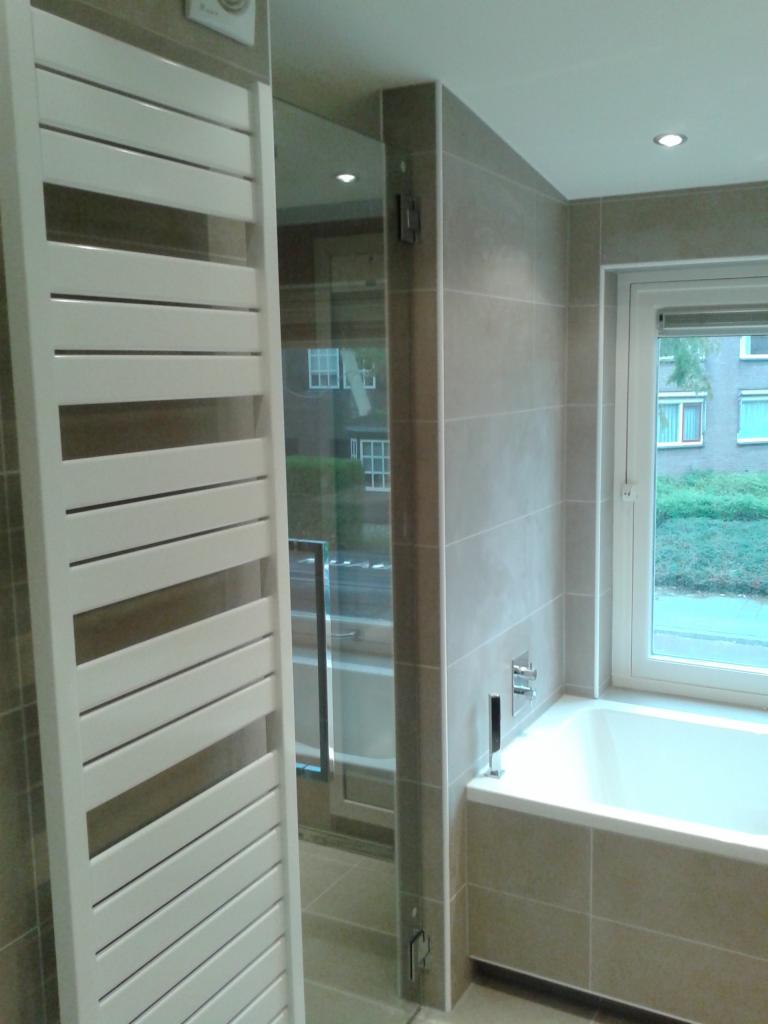 Nowoczesna łazienka z grzejnikiem drabinkowym, szklaną kabiną prysznicową i wanną pod oknem z widokiem na zieleń.