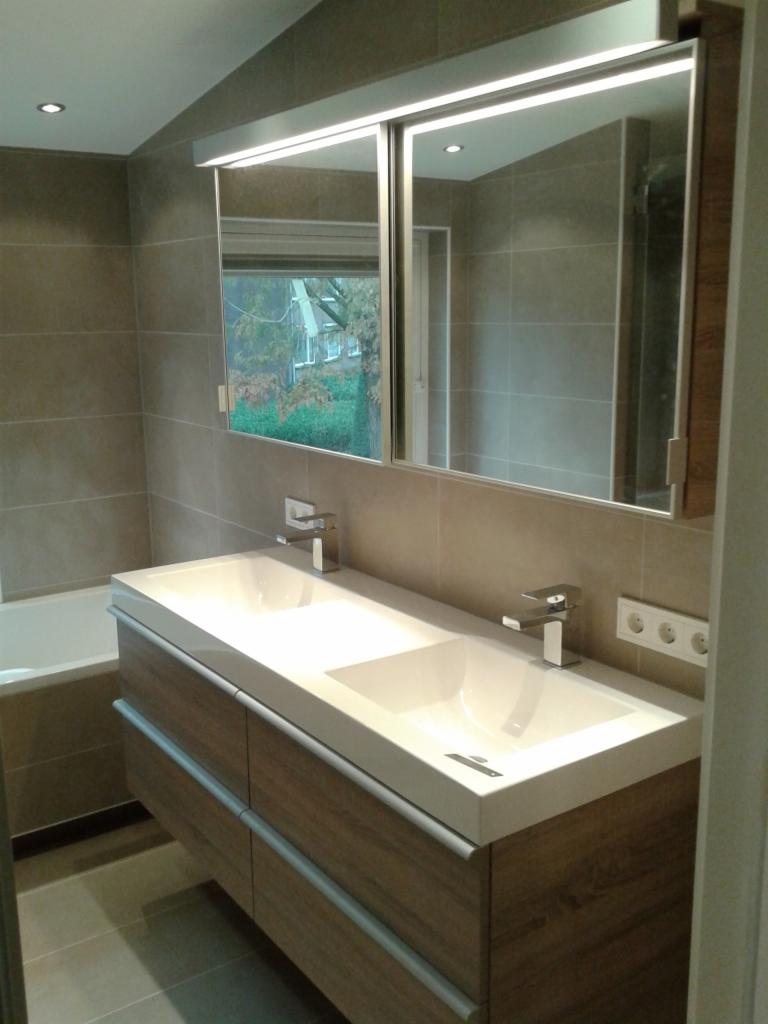 Nowoczesna łazienka z podwójną umywalką nablatową na szafce z drewnopodobnymi frontami i dużym lustrem z oświetleniem LED, widok na okno z zielenią.