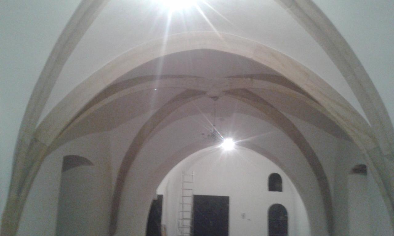 Wnętrze z łukowym sklepieniem, widoczna drabina oparta o ścianę, oświetlenie górne powoduje silne odblaski.