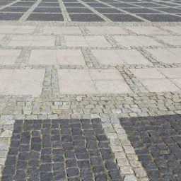 Nawierzchnia z szarej i czarnej kostki, ułożona w kwadratowy wzór z dużymi płytami pośrodku, widok z góry, w słoneczny dzień.