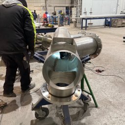 Pro-Weld Sp. z o.o. - Spawanie rur ze stali nierdzewnej na wózku transportowym w hali produkcyjnej. Widoczni spawacze w tle, narzędzia i elementy konstrukcyjne.