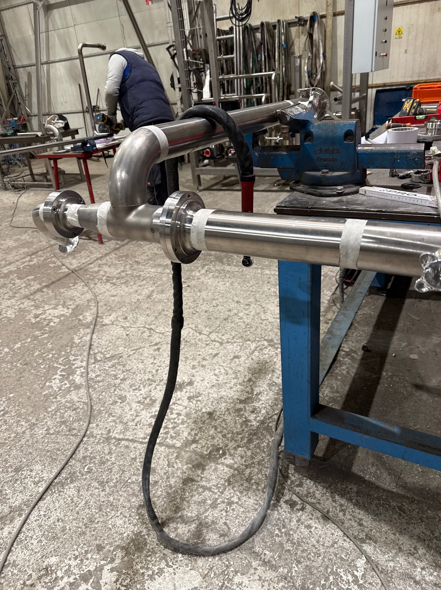 Spawanie rur ze stali nierdzewnej z flanszami na warsztacie. Widoczny spawacz i narzędzia. Element instalacji w trakcie montażu.