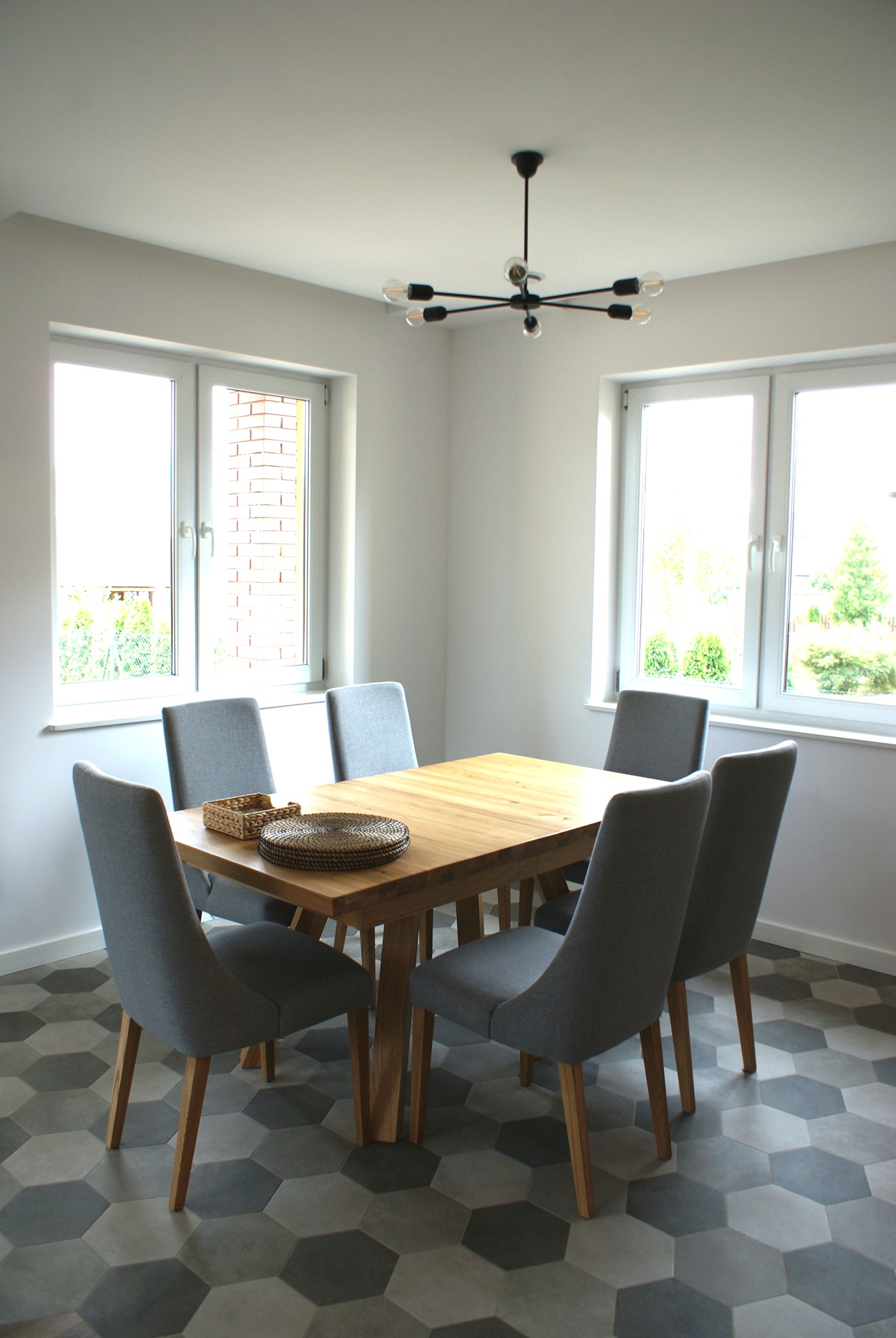Jasna jadalnia z drewnianym stołem, sześcioma szarymi krzesłami, heksagonalną podłogą i nowoczesną lampą wiszącą