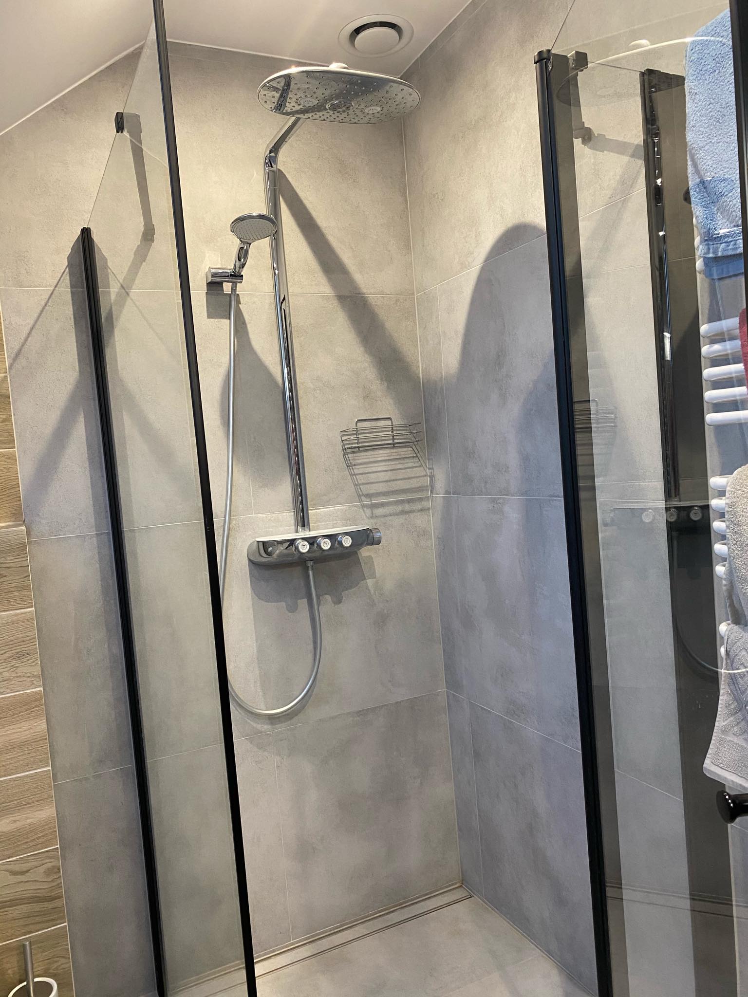 Nowoczesna kabina prysznicowa z deszczownicą i szklanymi drzwiami z czarnymi ramami, zamontowana w łazience w Gdyni z szarymi płytkami.