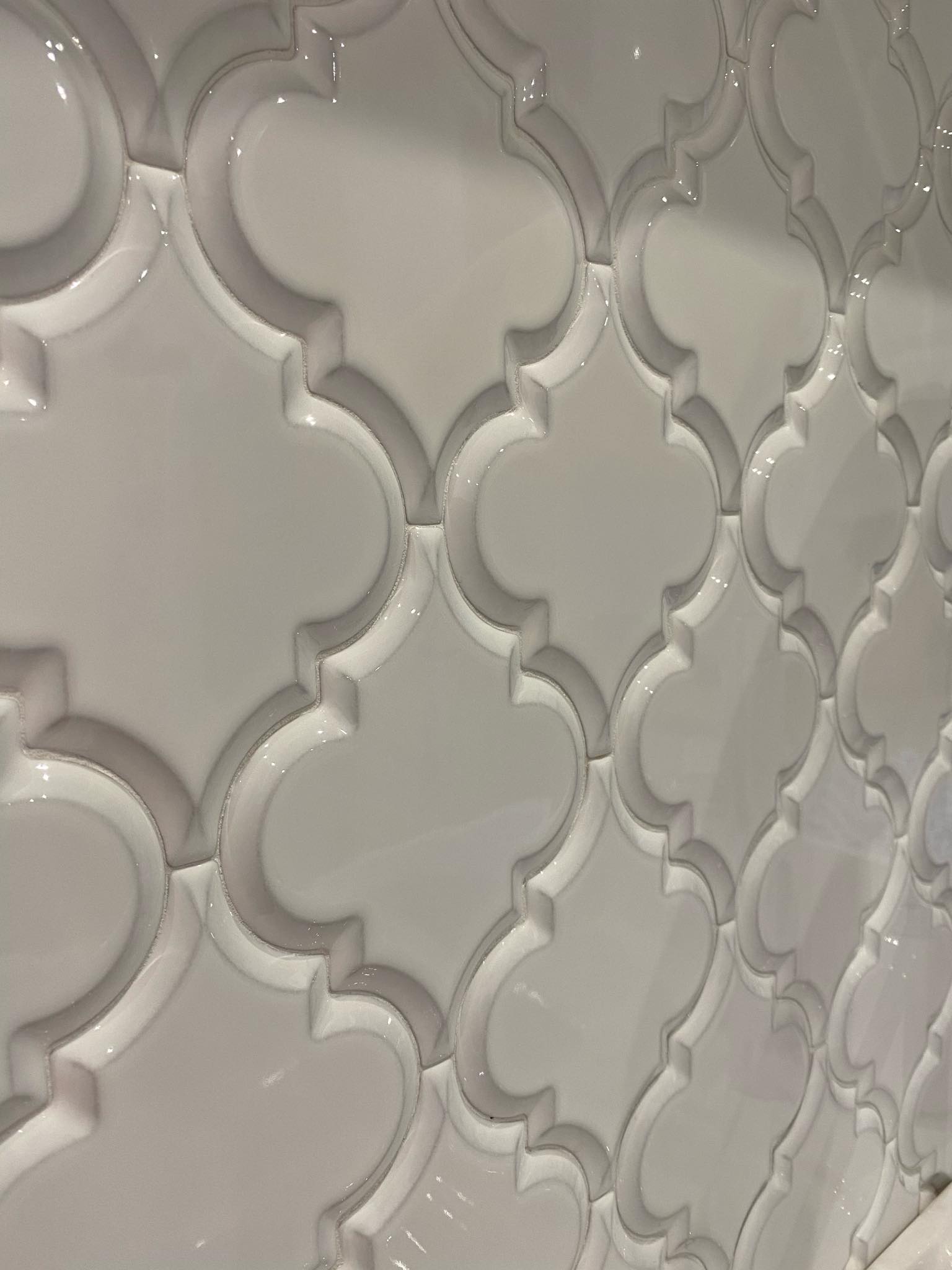 Błyszczące, białe płytki w marokańskim stylu, ułożone na ścianie, z widocznymi fugami, tworzące powtarzalny wzór.