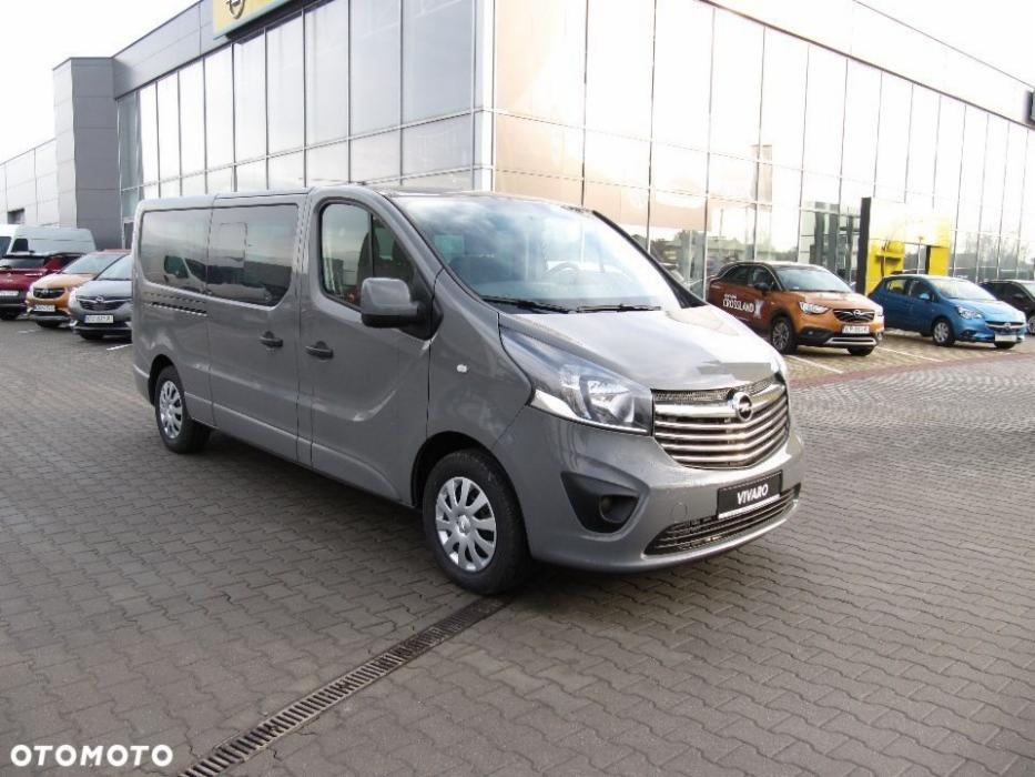 Szary Opel Vivaro, wersja przedłużona, zaparkowany na placu przed salonem samochodowym.
