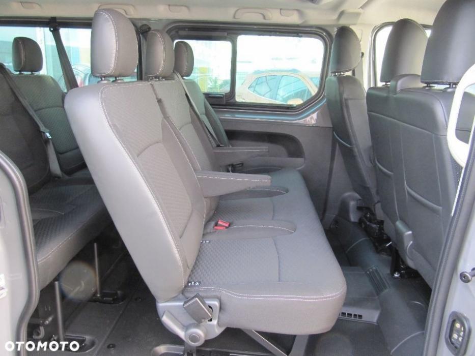 Wnętrze busa z szarymi fotelami pasażerskimi, widoczne zagłówki i pasy bezpieczeństwa, w tle okno z odbiciem innego pojazdu.