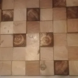 Dekoracyjna ściana z drewnianych kostek o zróżnicowanej kolorystyce i wyraźnych słojach drewna, tworzących trójwymiarową mozaikę.