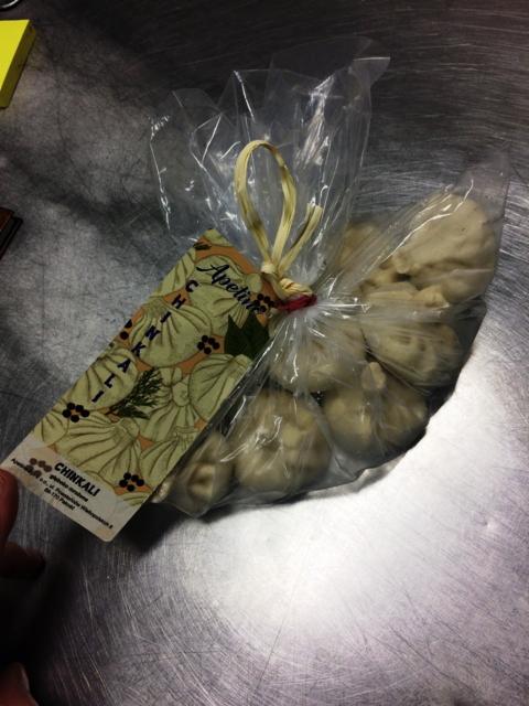 Pakiet chinkali w przezroczystej folii z etykietą, związany rafią na metalowej powierzchni.