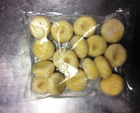 Mrożone, okrągłe pierogi leniwe w przezroczystym, plastikowym opakowaniu, na metalowej powierzchni.