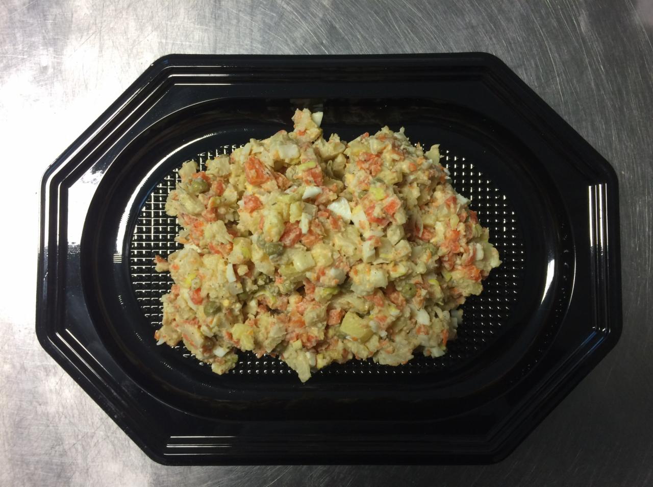 Sałatka jarzynowa z majonezem, jajkiem, marchewką i groszkiem, ułożona na czarnej, plastikowej tacy z kratką, na metalowym blacie.