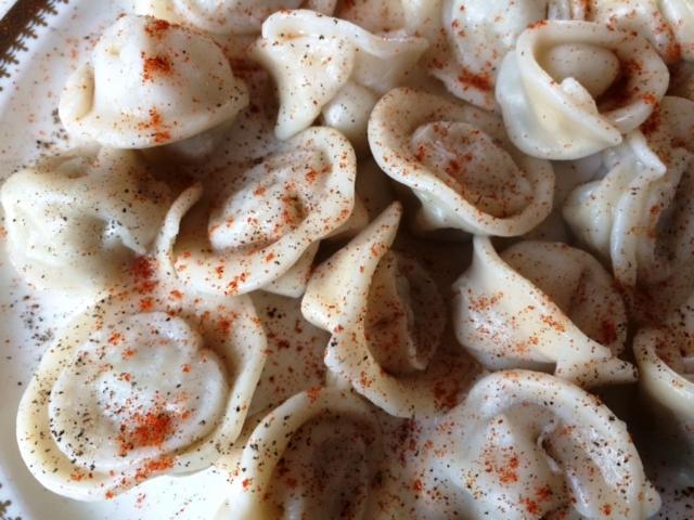 Bliski widok talerza z pierogami w białym sosie, posypanymi czarnym pieprzem i czerwoną papryką.