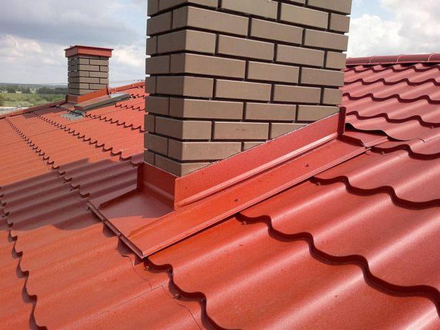 Czerwona blachodachówka z ceglanym kominem i obróbkami blacharskimi w kolorze dachu, widok z góry.
