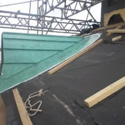 Montaż miedzianej lukarny na dachu pokrytym membraną, widoczne drewniane łaty i fragment rusztowania.