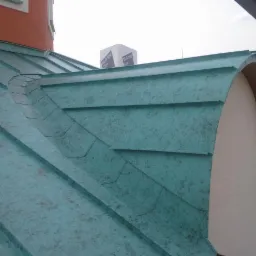 Nowe, miedziane pokrycie dachu z charakterystycznym patynowym wykończeniem, z detalami wykończeniowymi wokół lukarny dachowej.