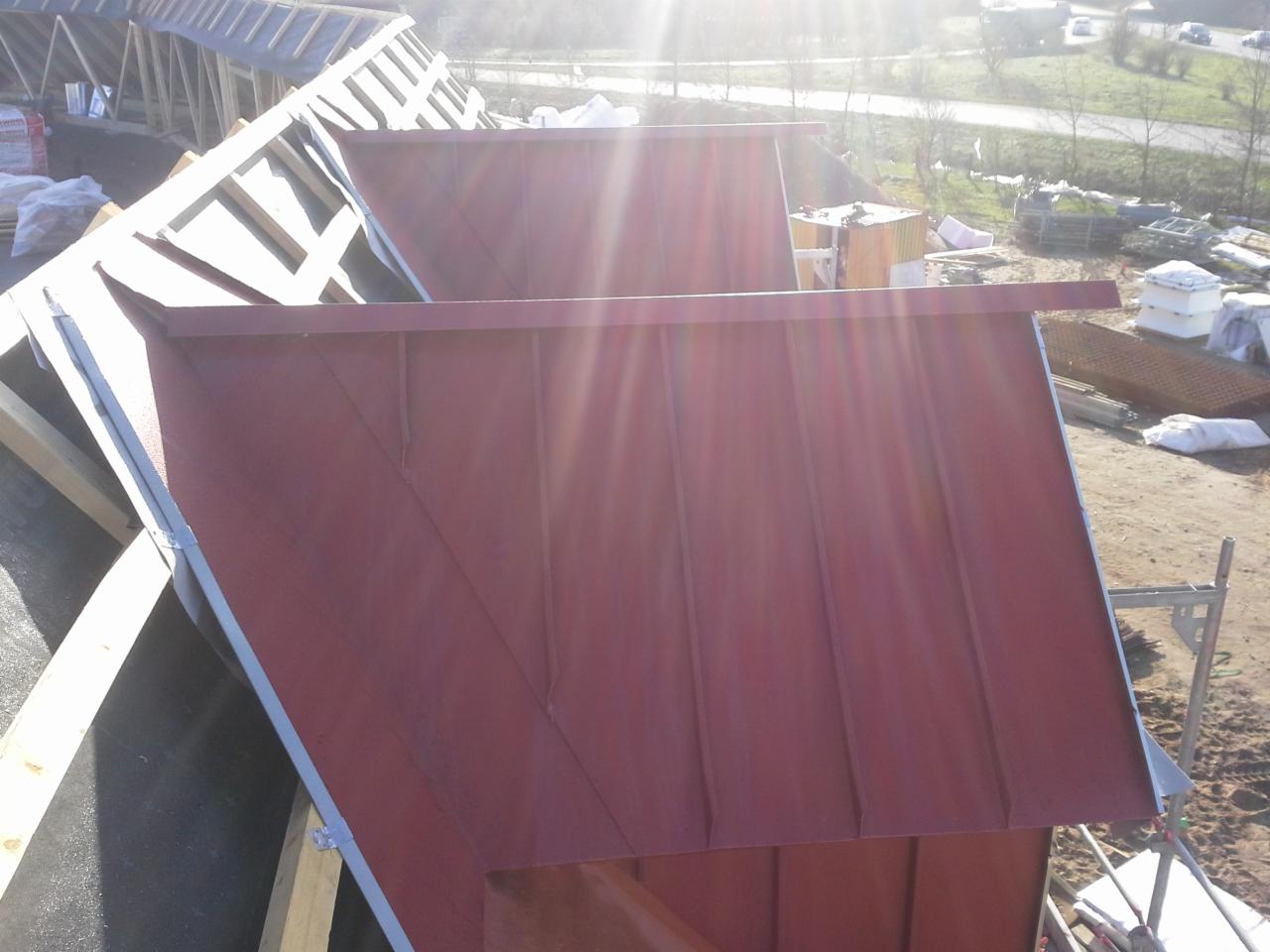 Czerwone metalowe panele dachowe z widocznymi łączeniami na nowo budowanym dachu z drewnianą konstrukcją, widok z góry w słoneczny dzień.