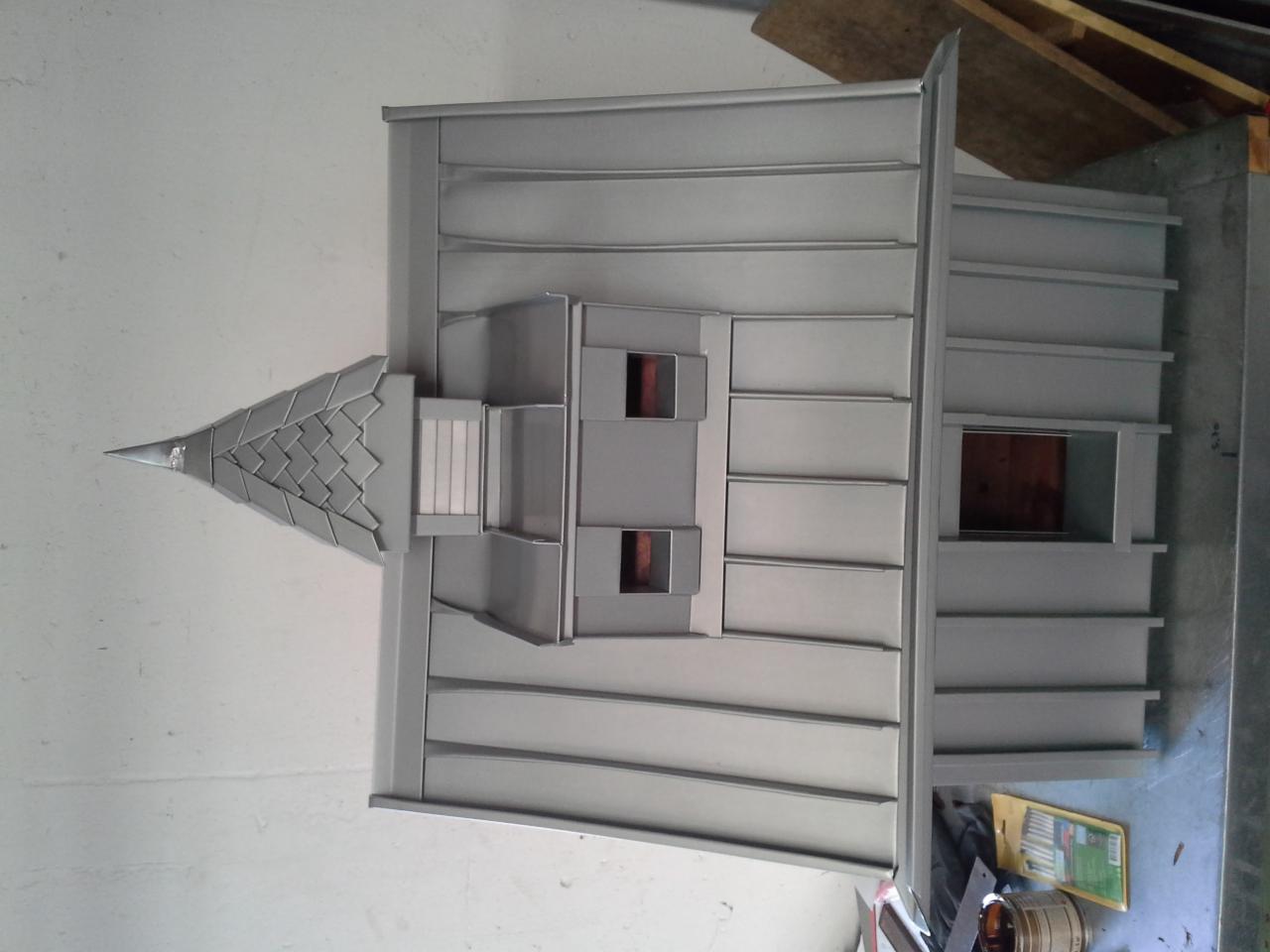 Model dachu z blachy w kolorze szarym, ukazujący detale konstrukcyjne, w tym obróbki przy oknach dachowych i wykończenie szczytu imitujące dachówkę.