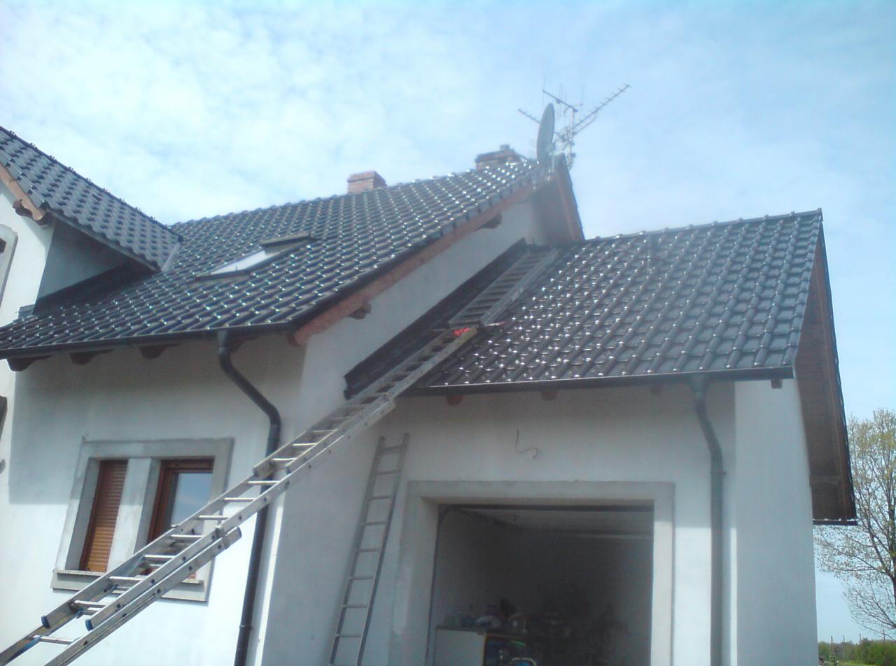 Nowy dach z czarnej dachówki ceramicznej na białym domu jednorodzinnym, widoczna drabina oparta o okap, antena satelitarna na szczycie dachu.