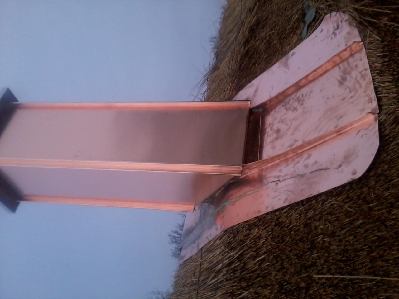 Miedziana listwa okapowa na strzechowym dachu, widoczne detale łączenia blachy i faktura słomy, niebieskawe niebo w tle.