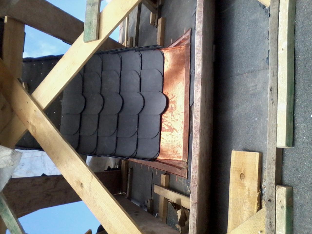 Fragment dachu w trakcie układania z łupka, widoczna konstrukcja drewniana i blacha okapowa z miedzi.