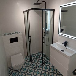 Usługi remontowo-budowlane Piotr Piosicki - Biała łazienka z kabiną prysznicową typu walk-in, umywalką na szafce i podświetlanym lustrem. Uwagę zwracają wzorzyste płytki podłogowe w stylu retro.