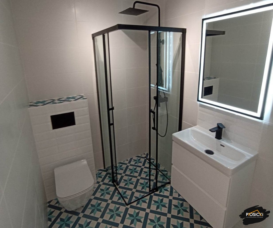 Biała łazienka z kabiną prysznicową typu walk-in, umywalką na szafce i podświetlanym lustrem. Uwagę zwracają wzorzyste płytki podłogowe w stylu retro.