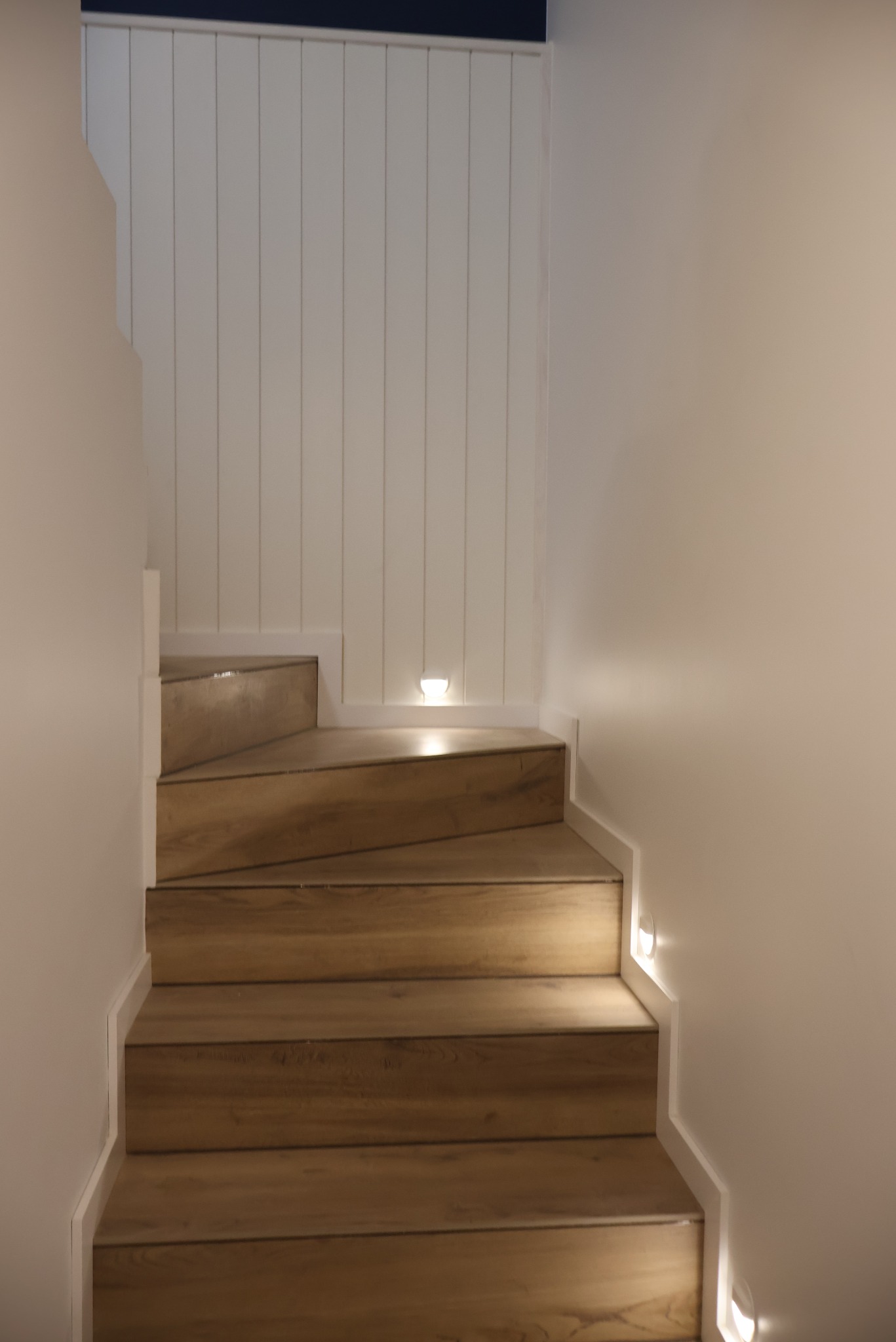 Drewniane schody z oświetleniem punktowym wzdłuż ściany i panelami ściennymi. Nowoczesne wykończenie wnętrza domu, minimalistyczny design.