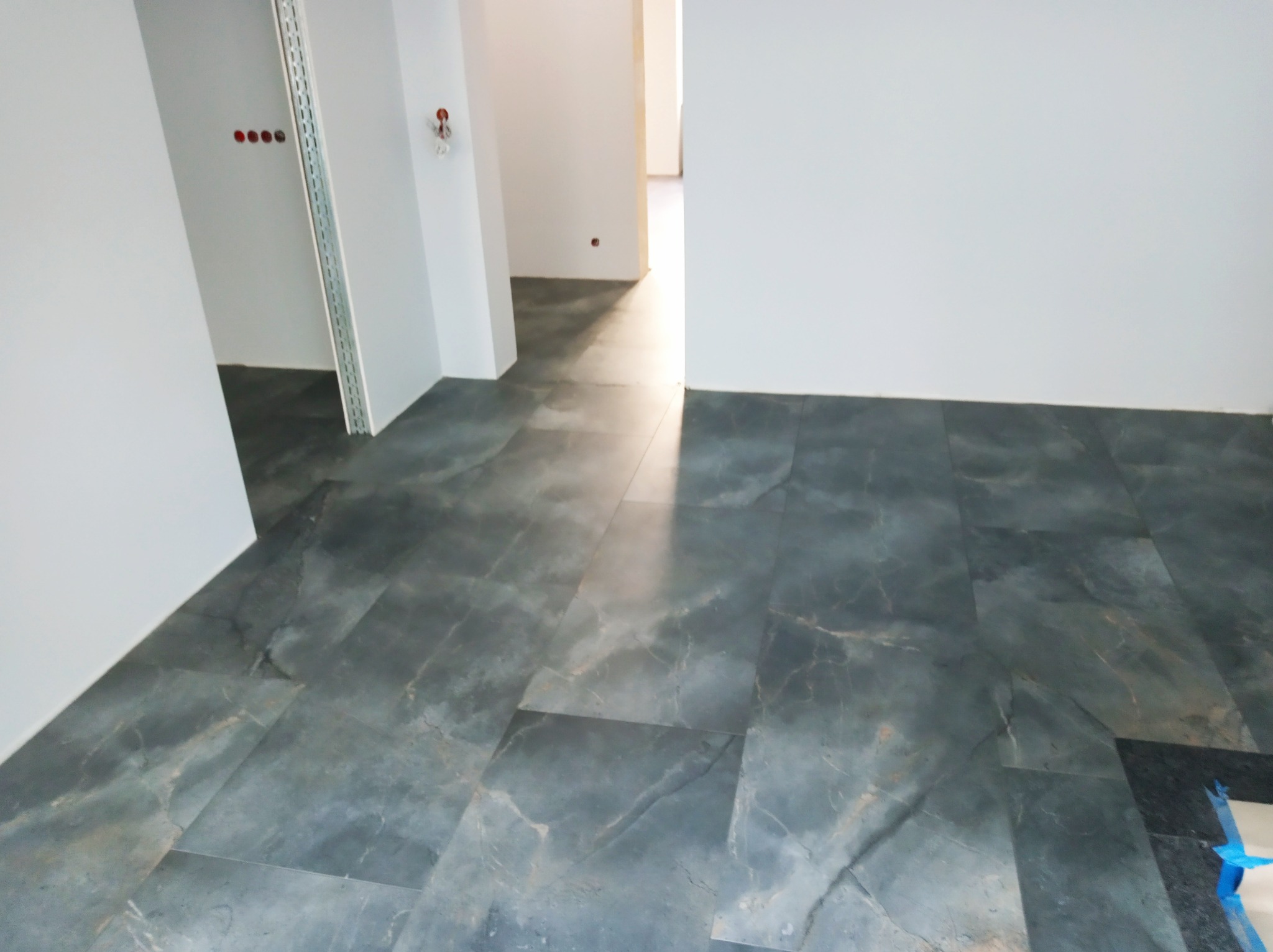 Ułożona podłoga z płytek imitujących marmur w odcieniach szarości, widok z perspektywy podłogi, białe ściany, wnętrze w trakcie wykańczania.