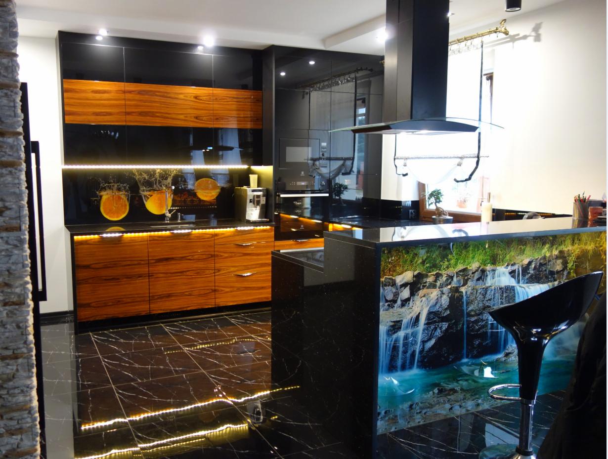 Nowoczesna kuchnia z czarnymi lakierowanymi frontami szafek górnych, drewnopodobnymi frontami szafek dolnych z podświetleniem LED, czarnym blatem i wyspą z motywem wodospadu, na podłodze czarne...