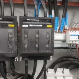 Rozdzielnia elektryczna z bezpiecznikami topikowymi i wyłącznikami różnicowoprądowymi, okablowanie w peszlach, widoczne oznaczenia Zasilanie UPS i Zasilanie By-Pass.